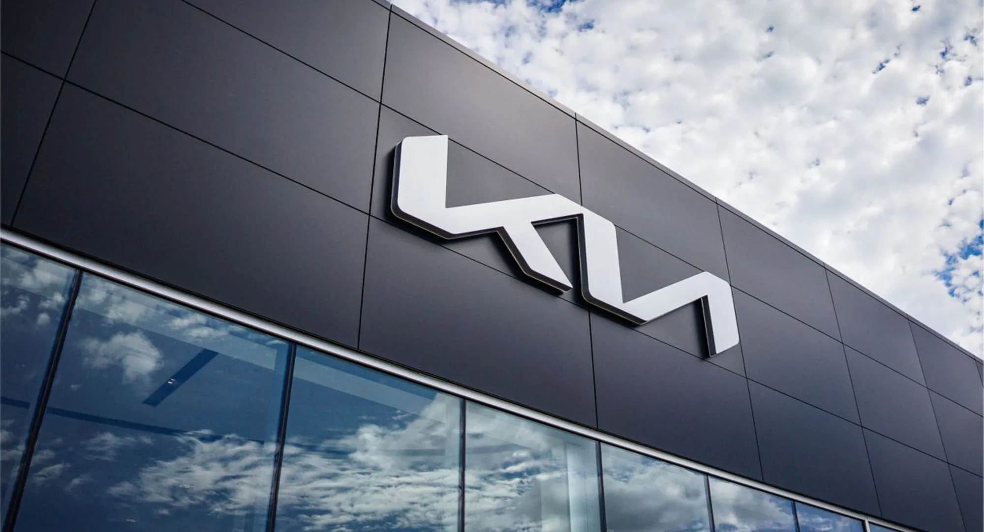 KIA logo mounted on a cladded dealership façade against a blue sky