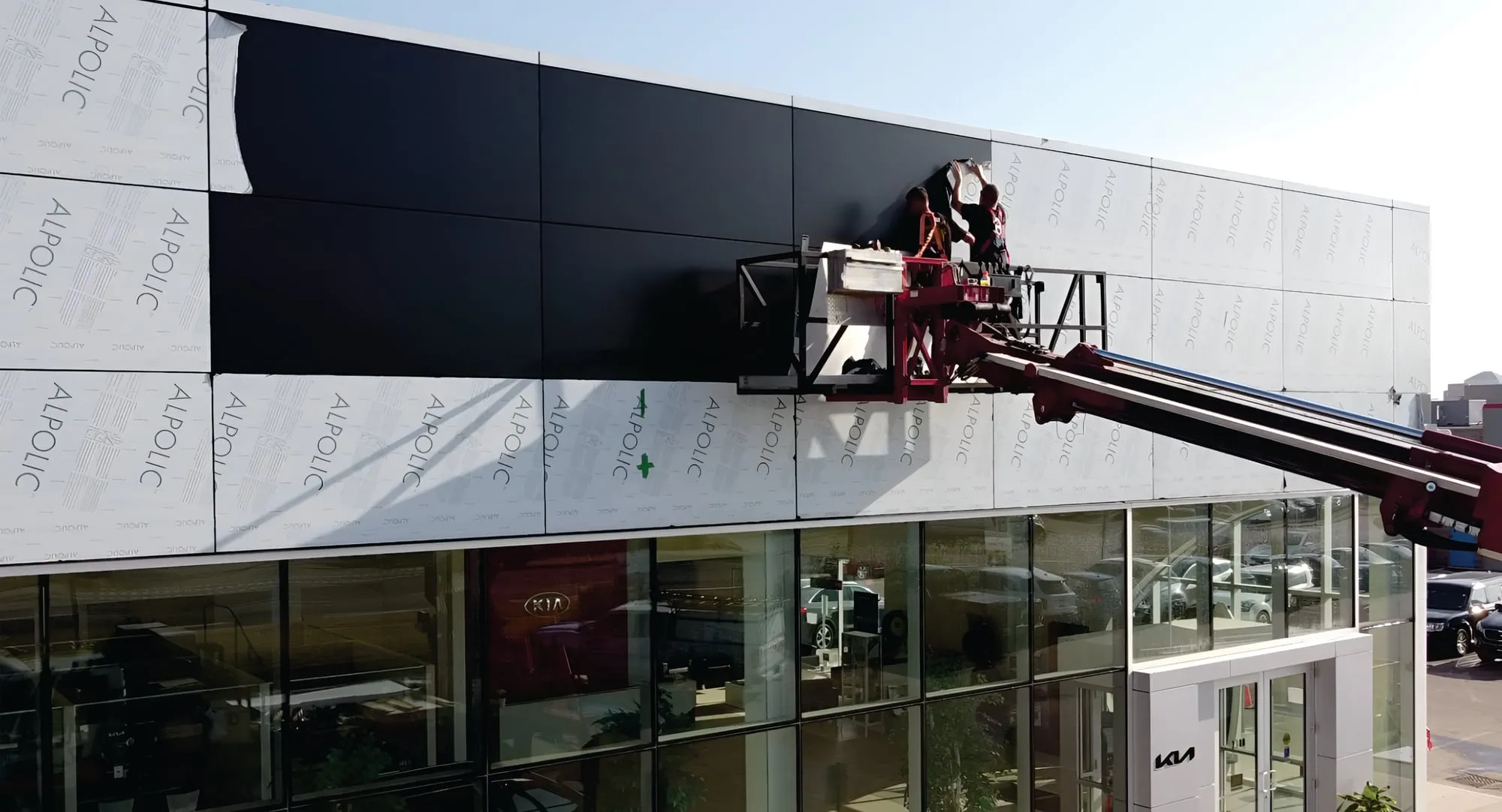 Crew installing architectural cladding panels on a dealership façade from a boom lift