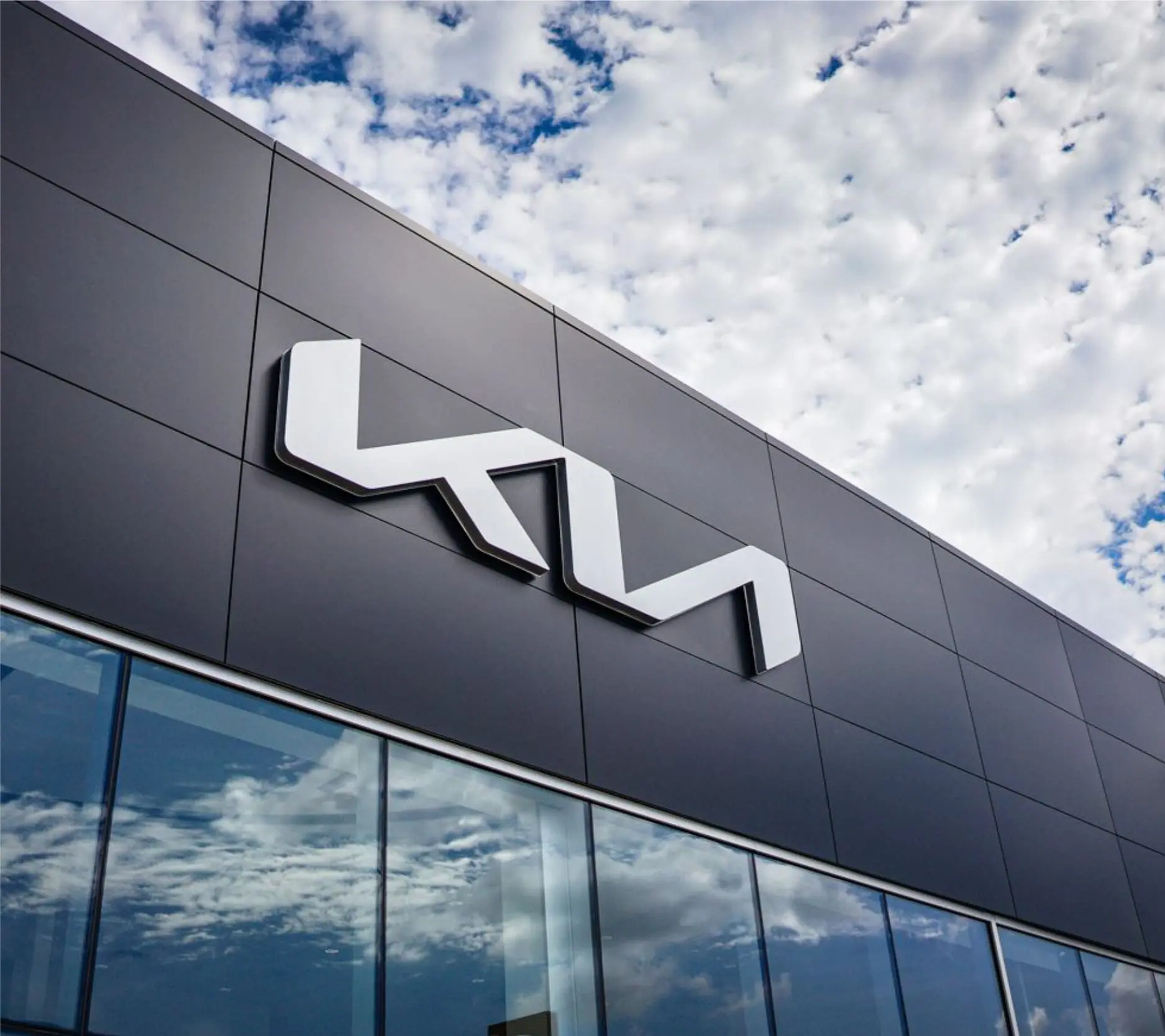 KIA dealership façade with dimensional white logo on dark architectural cladding