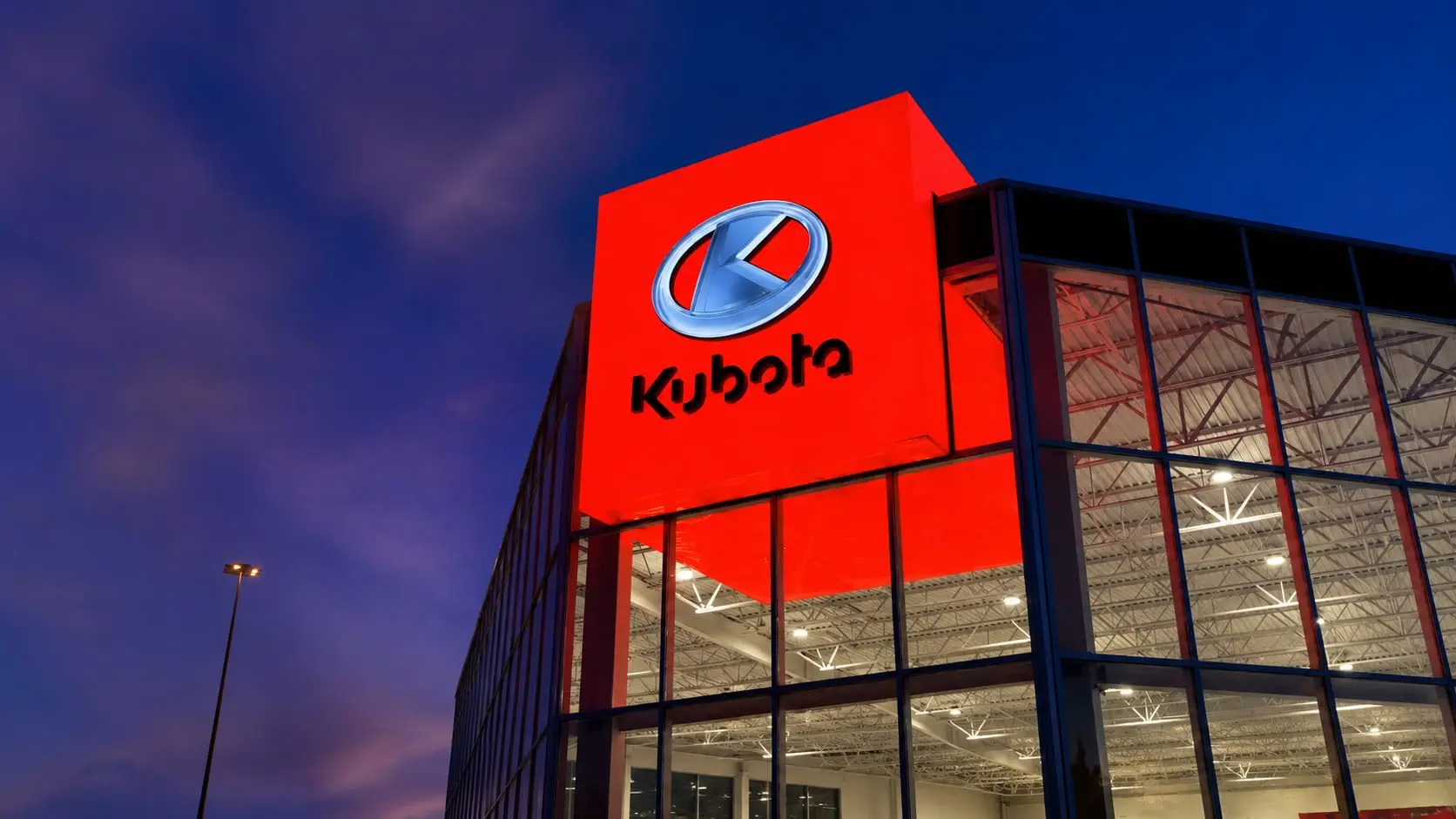 Illuminated red Kubota cube extending through the dealership façade at dusk