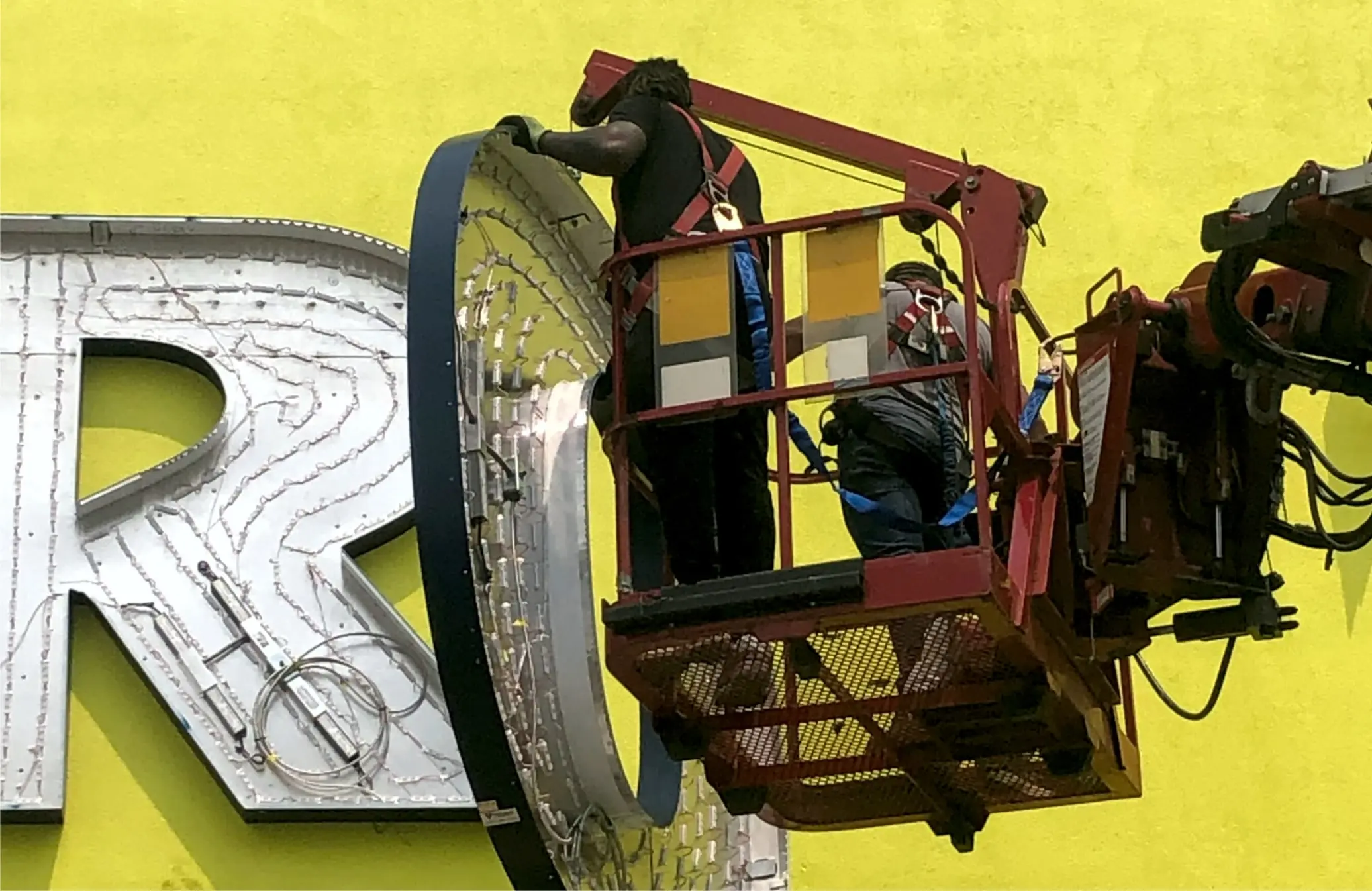 Installation crew in a boom lift fitting a large channel letter to a building façade