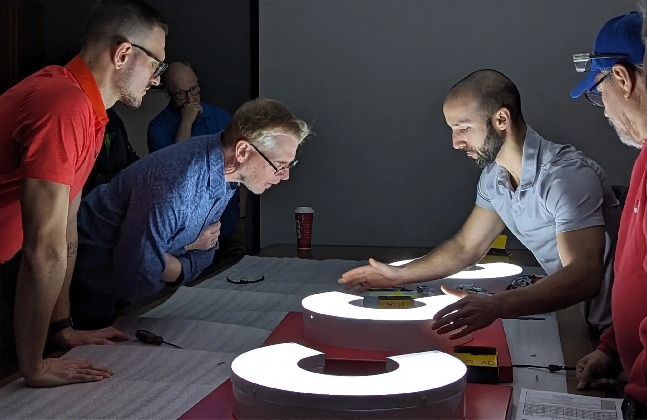 Pride Visual Solutions team reviewing an illuminated channel letter sample together on the layout table